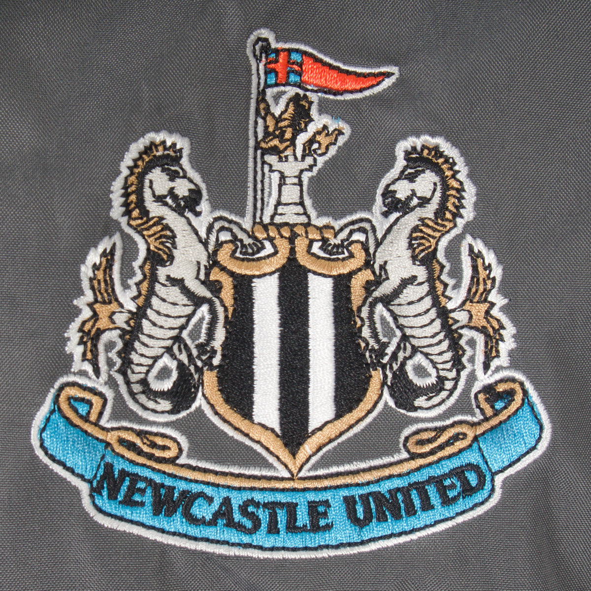 Newcastle Utd adults shower jacket in black & grey with club crest to chest .