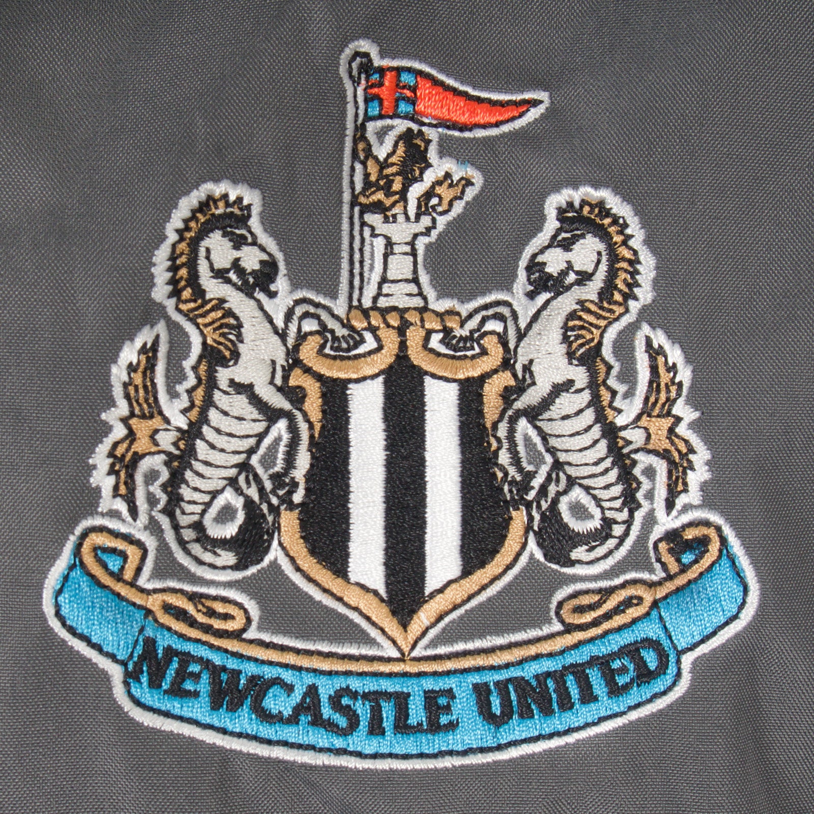 Newcastle Utd adults shower jacket in black & grey with club crest to chest .