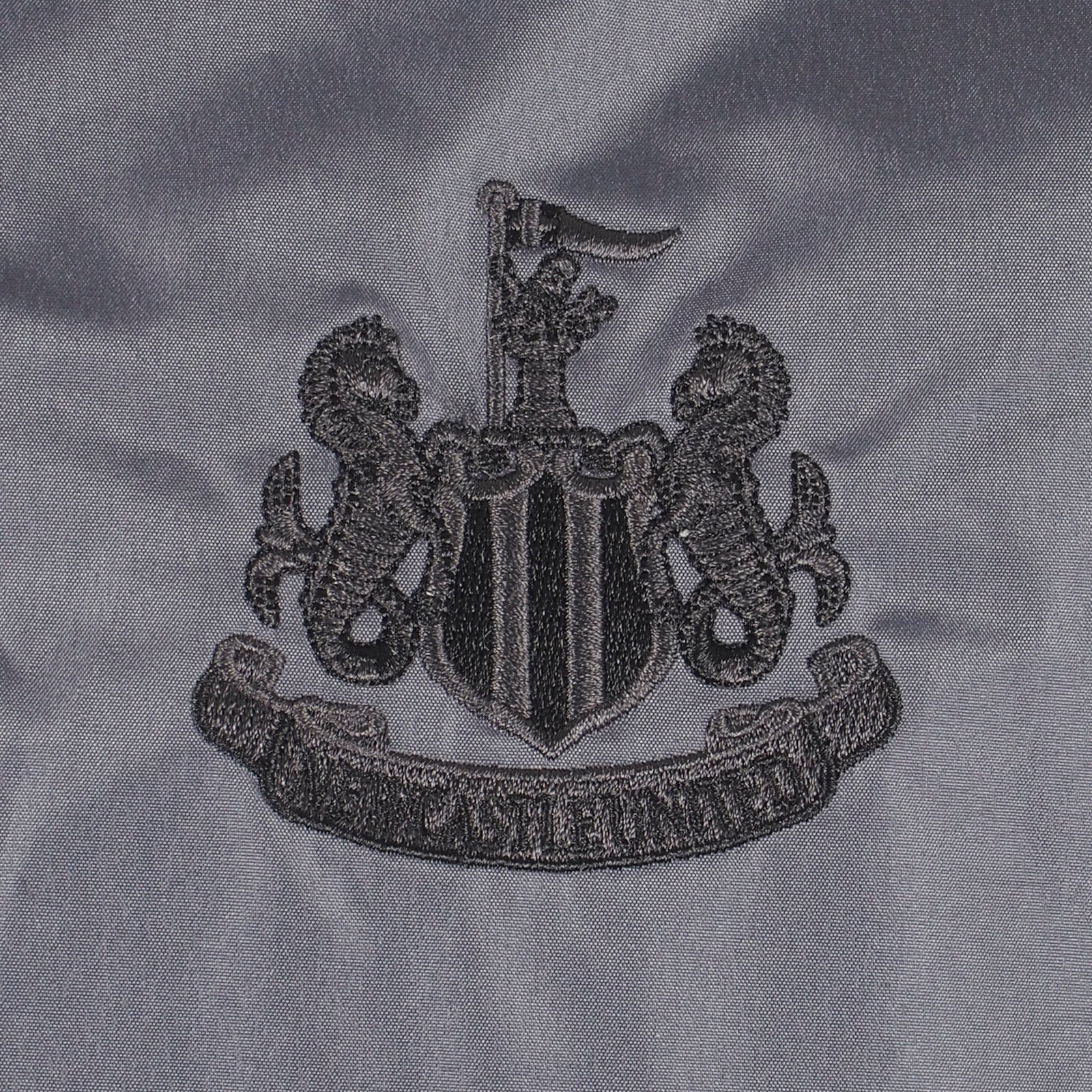 Newcastle Utd adults hooded shower jacket in grey with club crest to chest .